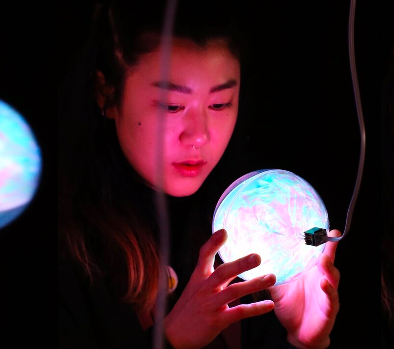 A photo of a person tilting and reading a pink and blue orb.